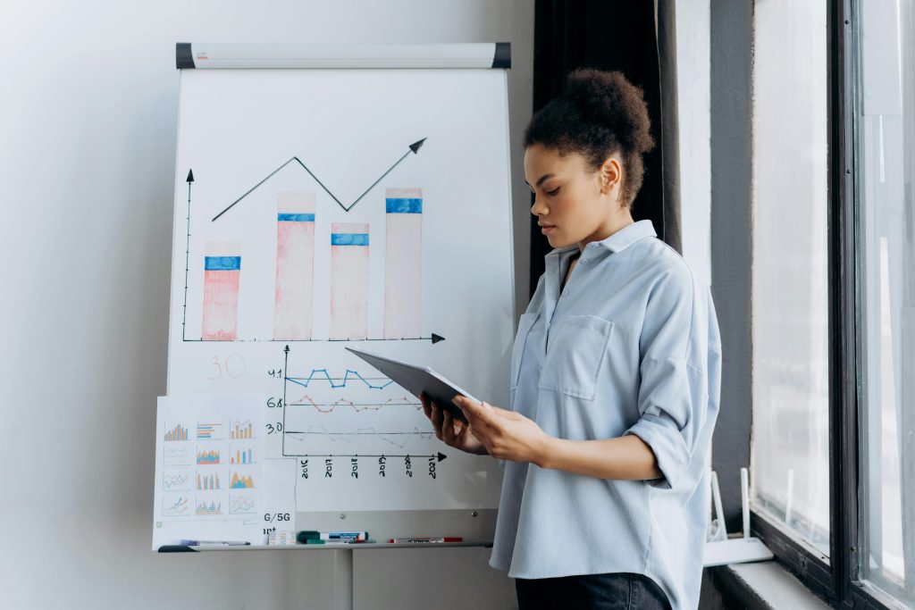 A woman analyzing sales data on a tablet next to a presentation board with graphs.