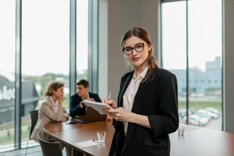 Confident businesswoman holding notebook during meeting in modern office setting.